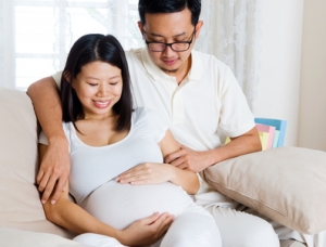 Asian man and his pregnant wife sitting on sofa